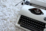 A vintage typewriter with a sheet of paper half-typed, resting on a wooden desk.