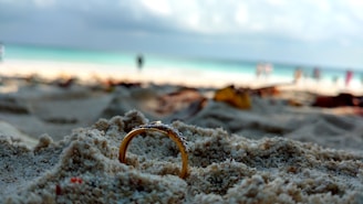Close-up of a sparkling silver ring partially buried in the sand beside a metal detector.