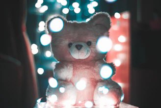 A soft teddy bear sitting cozily among other plush toys in a bright corner.