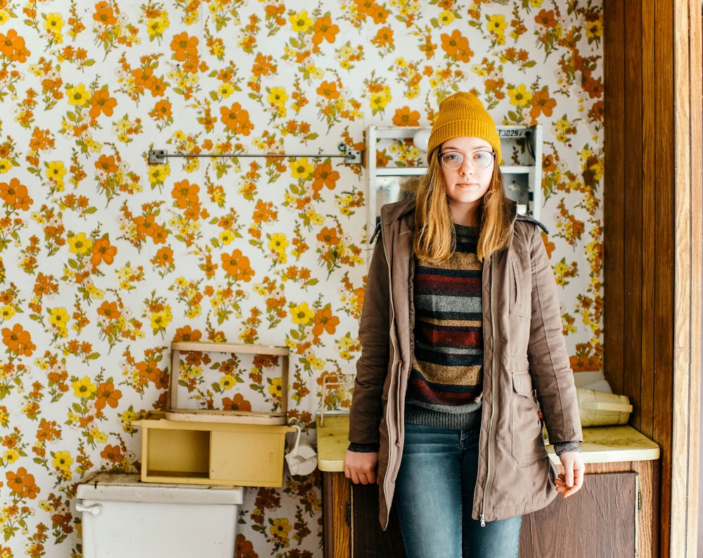 woman standing near cabinet in front of floral wallpaper