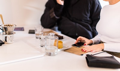 woman holding smartphone beside clear drinking glass on table bloom google meet background