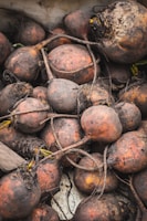 A pile of freshly harvested beets with earthy roots and dirt-covered skins. The beets vary in size and display natural imperfections and textures.