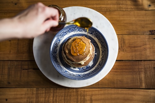 A wooden spoon drizzling syrup over pancakes.