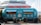A retro-style turquoise food truck is parked in front of a building. The truck has vibrant red illuminated letters on top spelling out 'BRATYA GRILL' in Cyrillic. The sides of the truck are adorned with illustrations and names of different burger options, including Lucky, Killer, Chicken, Asia, Mona Lisa, Vegan, and Cowboy. Three wooden tables with metal barrels as bases are placed in front of the truck.