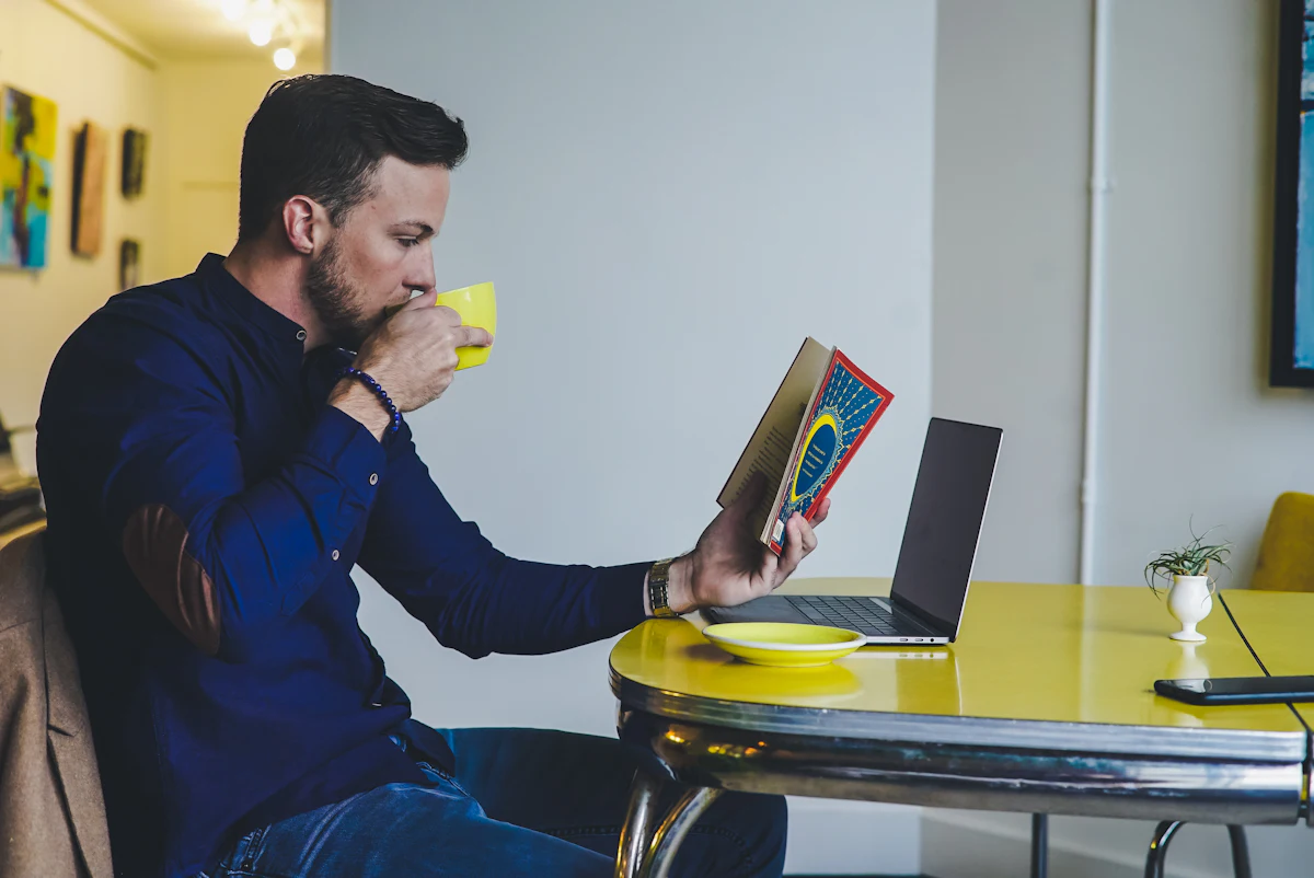 A person reading a book and drinking a beverage, representing focused practice and deliberate self-improvement