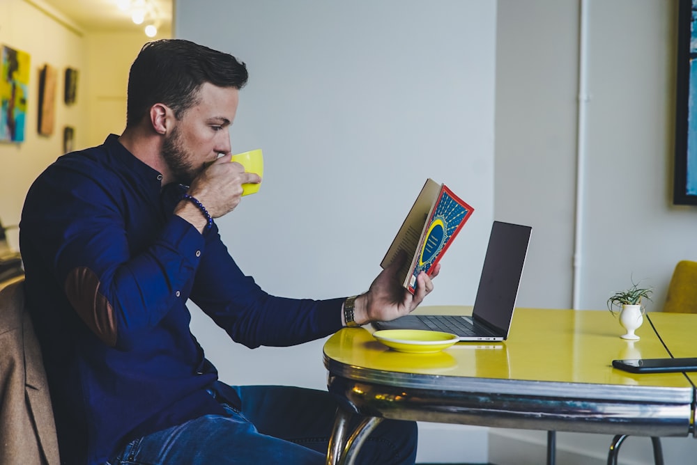 Man reading a book at a table whilst drinking coffee