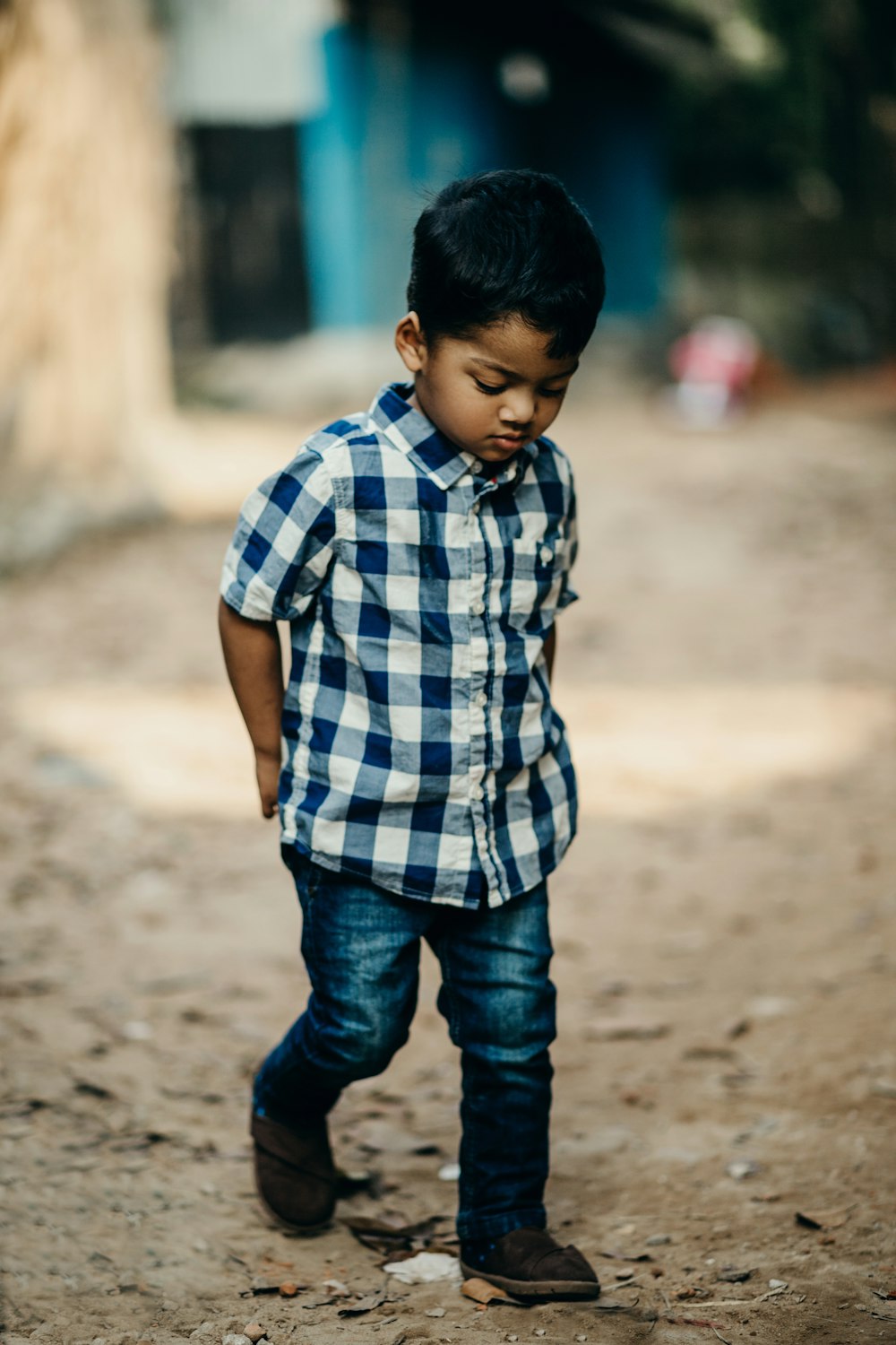 Photographie sélective de mise au point d’un garçon en chemise boutonnée à carreaux bleu et blanc regardant vers le bas
