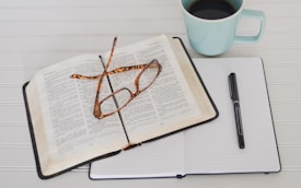 flat lay photography of tortoiseshell eyeglasses on top of the Bible near black pen and teal mug