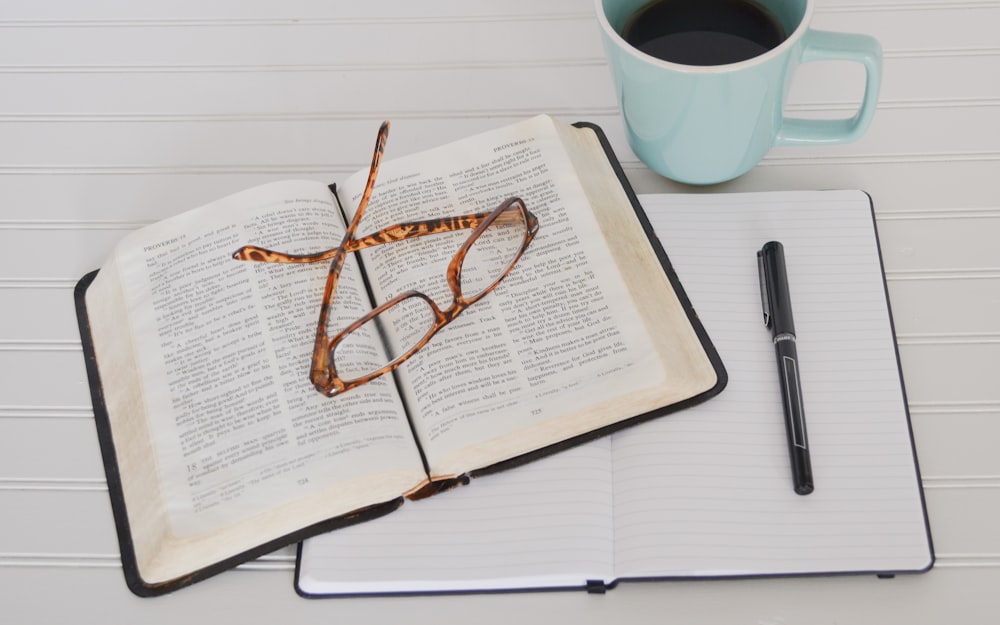 flat lay photography of tortoiseshell eyeglasses on top of book near black pen and teal mug