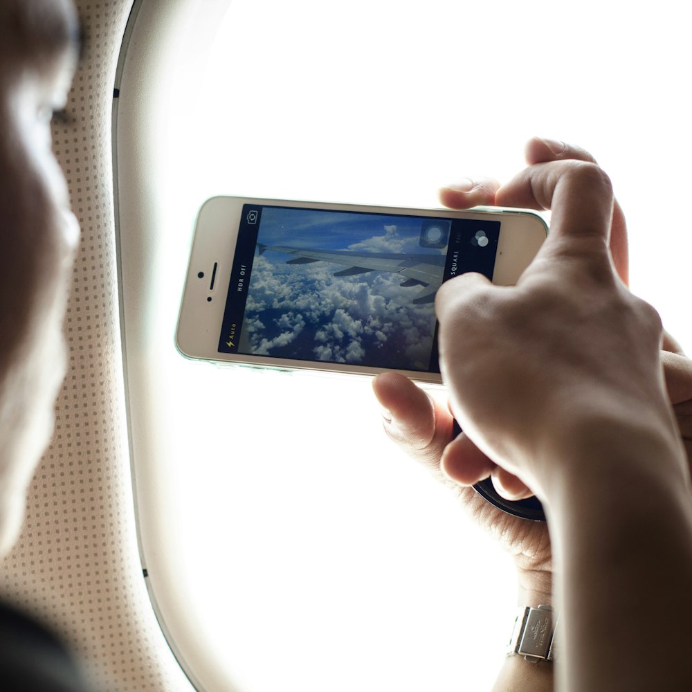 pessoa segurando o telefone tirando foto da asa do avião