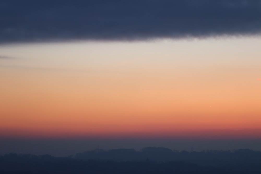 Silhouette von Bergen unter grauem und orangefarbenem Himmel bei Sonnenuntergang