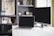 A modern workspace featuring a laptop and monitor on a white desk. The background includes a bookshelf filled with books and decorative items.