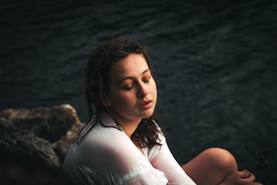 A serene woman sitting by the sea, eyes closed, embracing calmness.