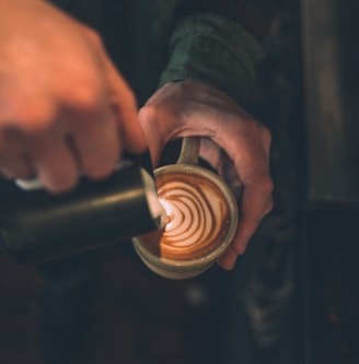 man pouring latte art to cup filled with coffee