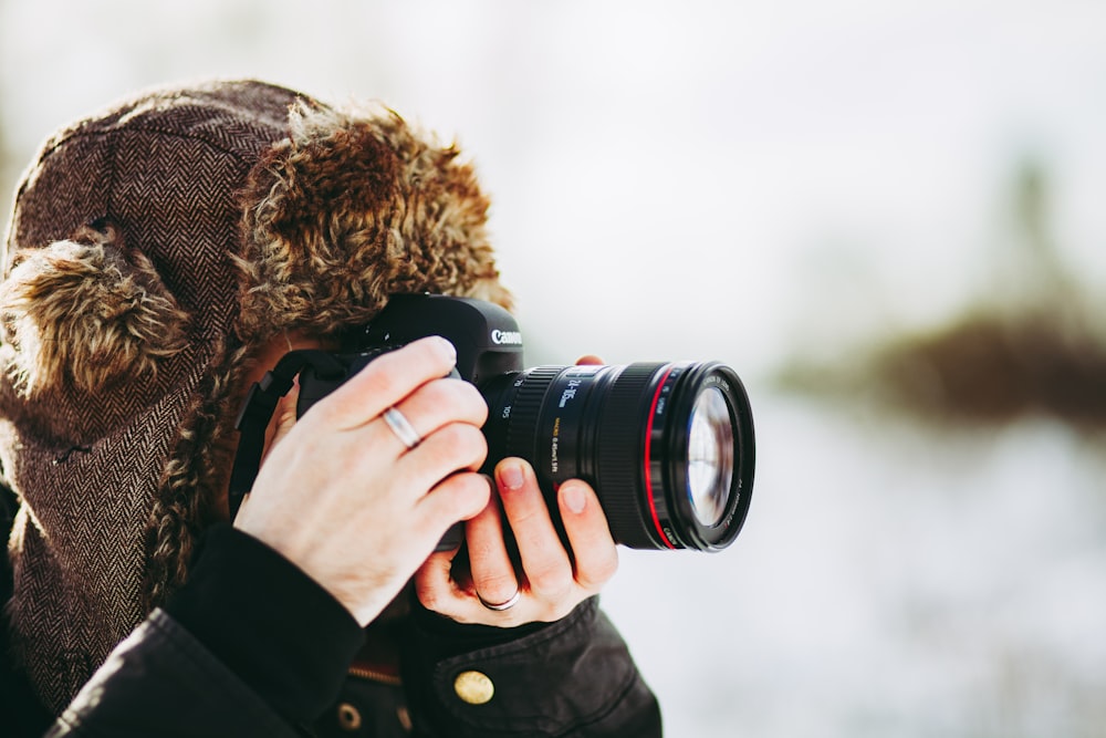 person wearing bomber hat and using black camera