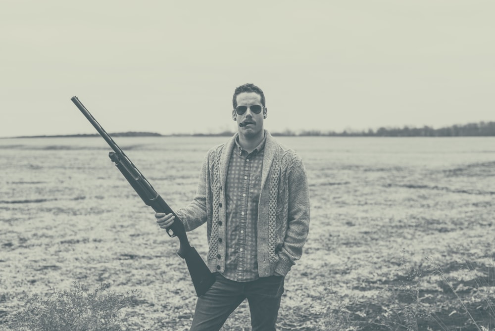 grayscale photography of man holding rifle