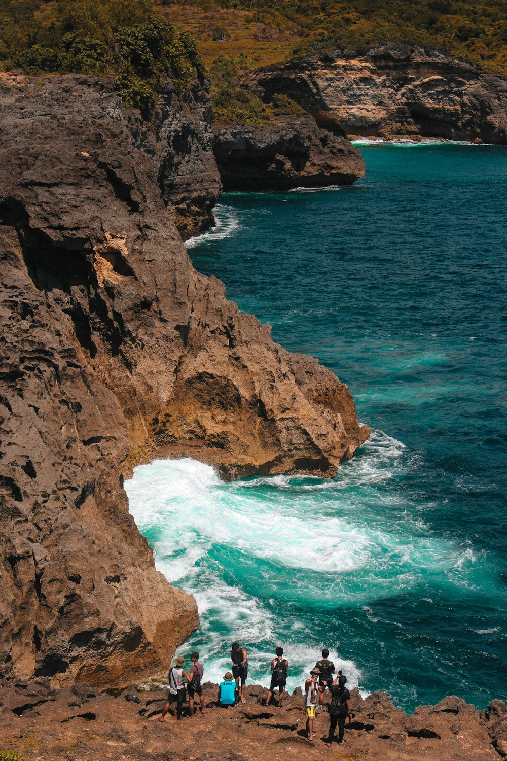 people standing on mountain cliff facing body of water