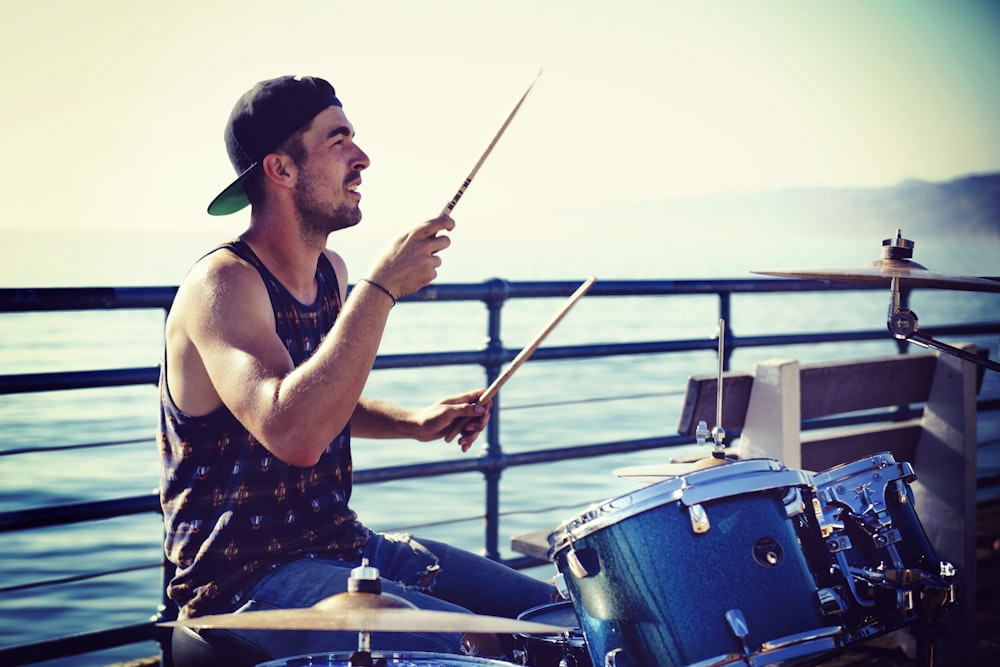 man sitting and playing with drums near sea