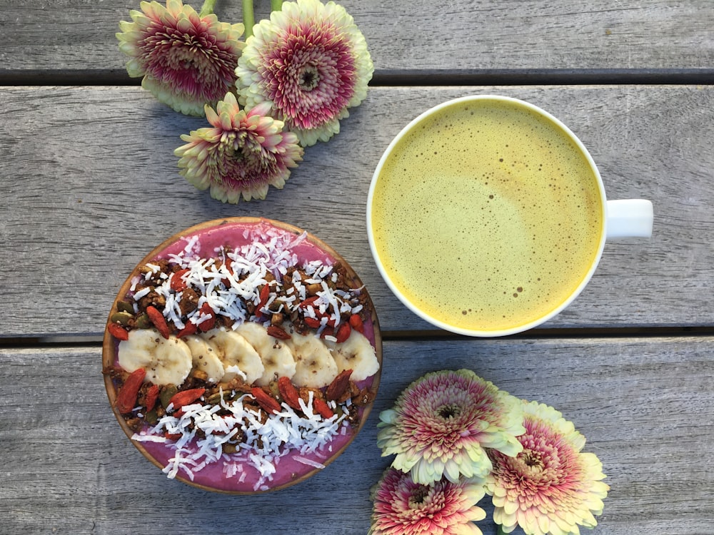 high angle photo of yellow liquid inside cup and dish with flowers