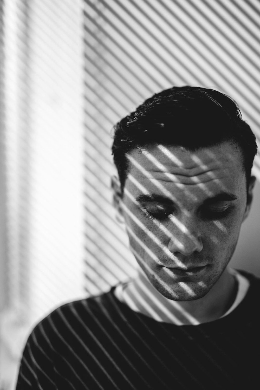 man looking down near window in grayscale photography