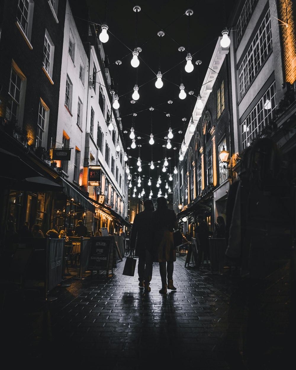 silhouette of couple walking under light bulbs between buildings