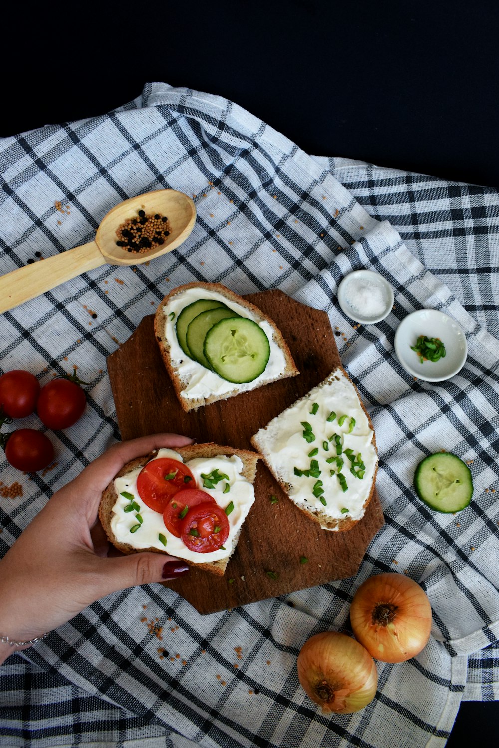 person holding sandwich near two sandwiches on chopping board