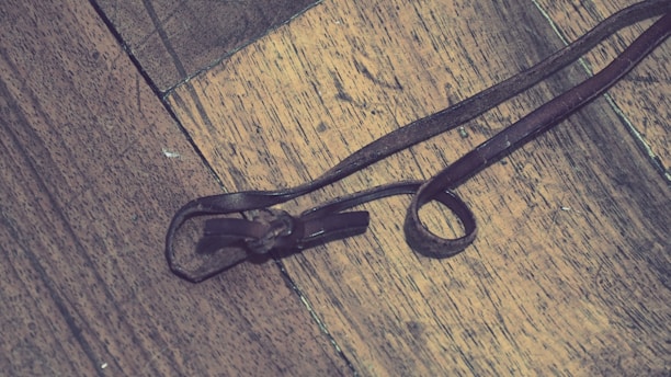 A close-up of a brown leather strap lying on a wooden surface, intricately tied into a loop.