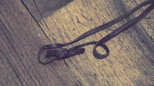A close-up of a brown leather strap lying on a wooden surface, intricately tied into a loop.