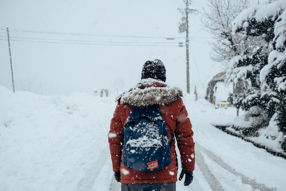 person wearing red jacket walking near tree during winter