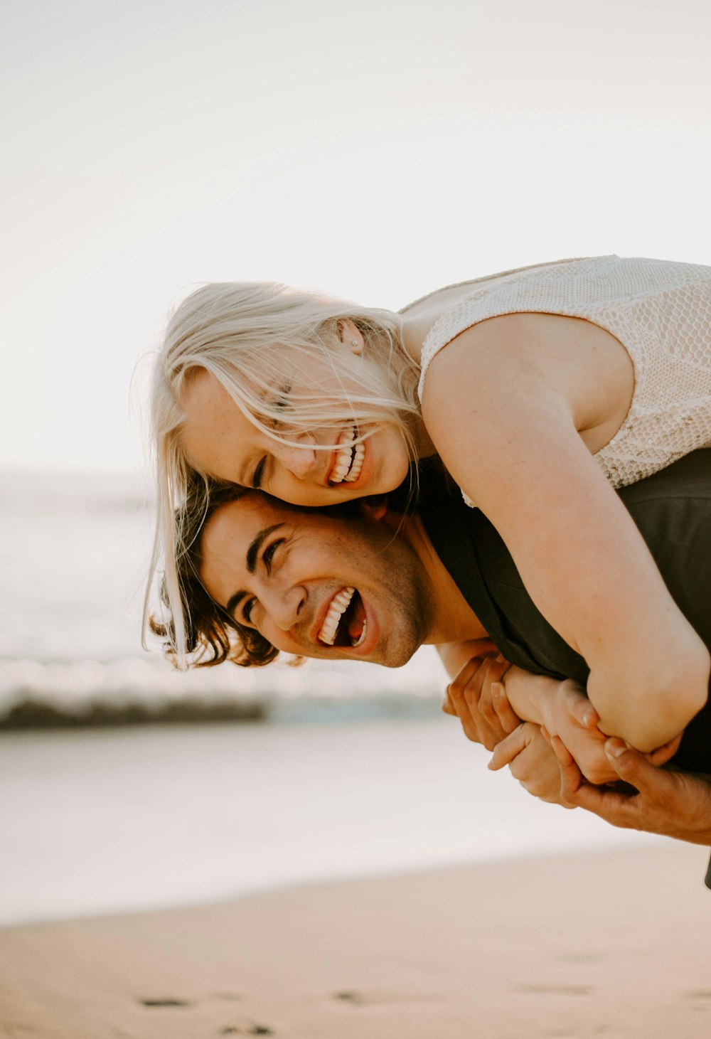 woman smiling while piggy riding on back of man on the beach