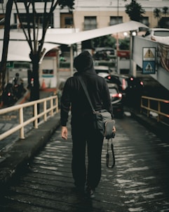 man in black hoodie holding DSLR camera walking on steep road
