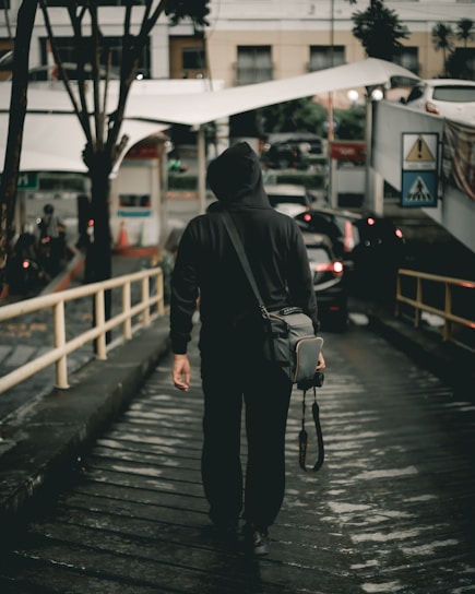 man in black hoodie holding DSLR camera walking on steep road