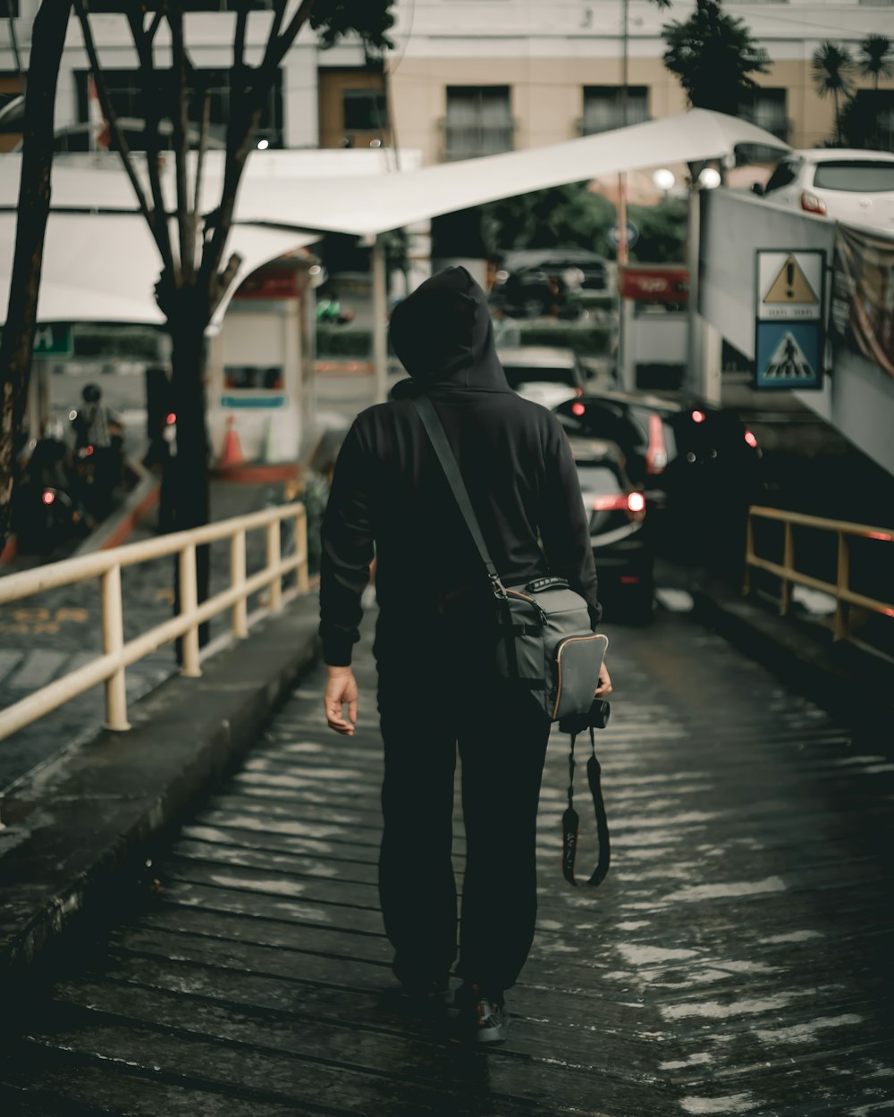 man in black hoodie holding DSLR camera walking on steep road