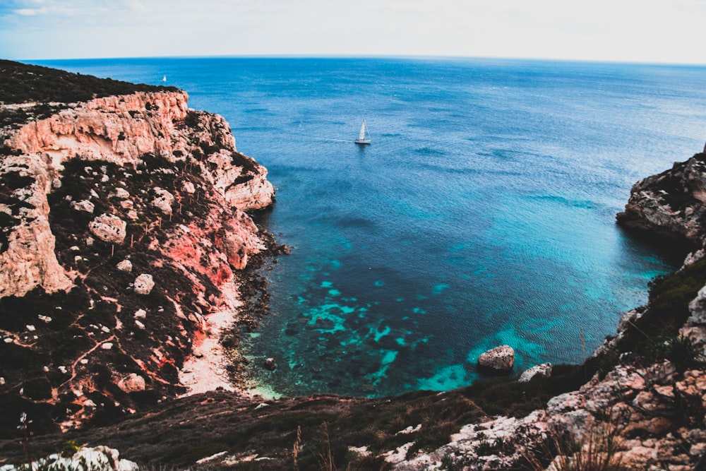 white boat on body of water near rock formation at daytime