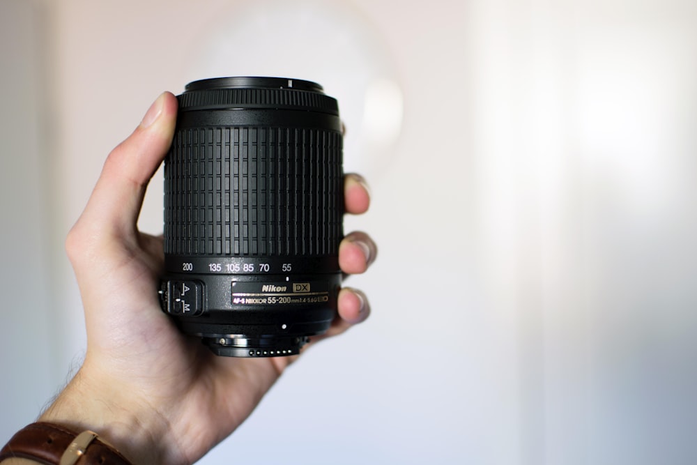 person holding black Nikon camera lens