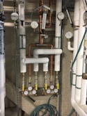 A complex arrangement of pipes, gauges, and valves typically found in a utility or maintenance room. The pipes are labeled for different water types, such as tempered water, domestic hot water, and domestic cold water. Several circular gauges display pressure readings, and there are multiple valves with yellow handles.