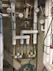 A complex arrangement of pipes, gauges, and valves typically found in a utility or maintenance room. The pipes are labeled for different water types, such as tempered water, domestic hot water, and domestic cold water. Several circular gauges display pressure readings, and there are multiple valves with yellow handles.