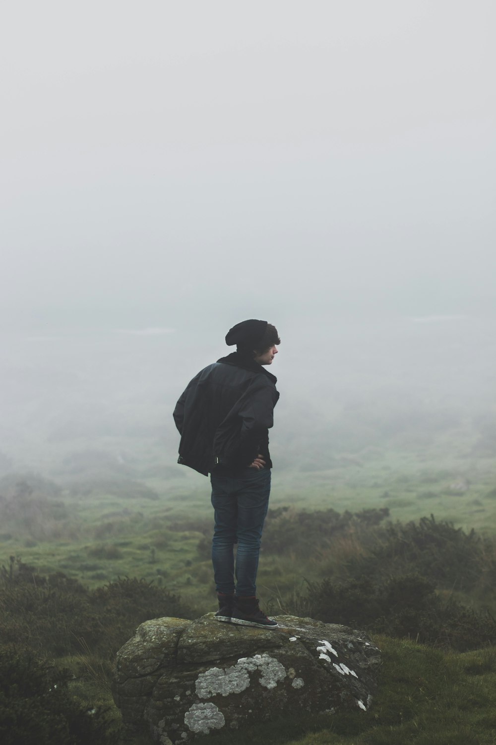 man wearing black jacket standing on rock