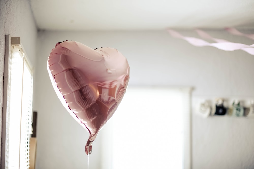 balão rosa em forma de coração perto das persianas da janela