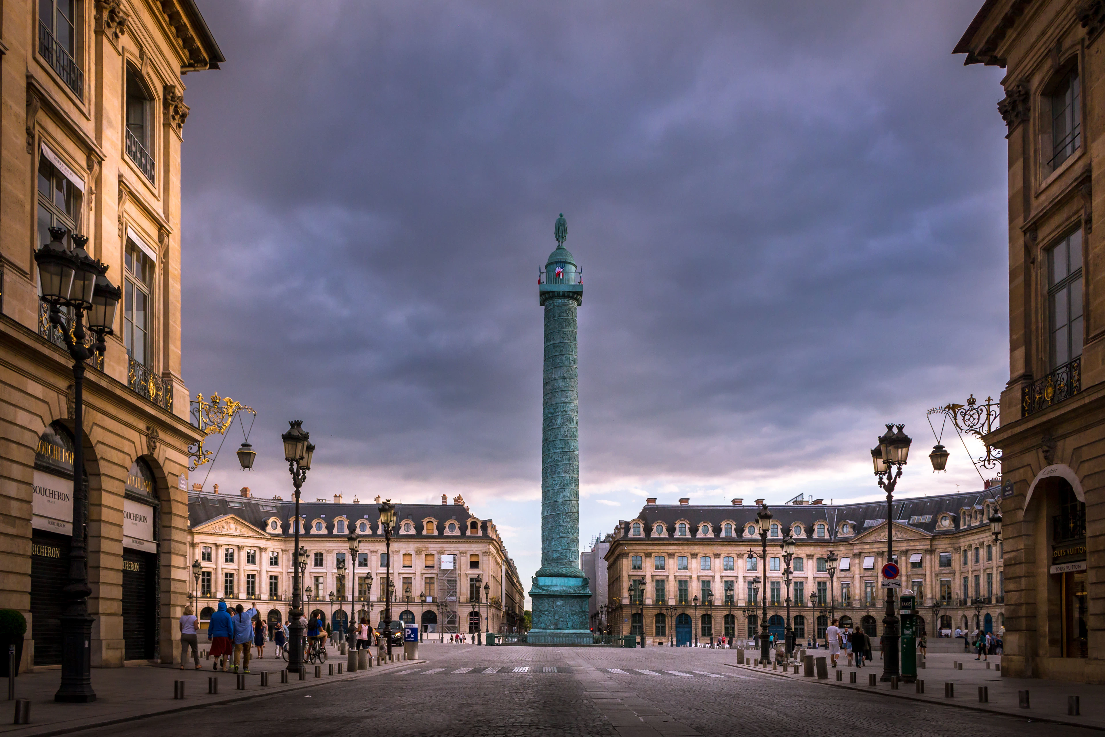 Place Vendôme's bronze column beneath a stormy dusk sky, framed by golden-lit facades.