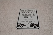 A parking sign attached to a textured wall, indicating reserved parking for tenants only. It warns that violators will be towed and features a graphic of a tow truck.