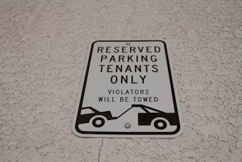 A parking sign attached to a textured wall, indicating reserved parking for tenants only. It warns that violators will be towed and features a graphic of a tow truck.