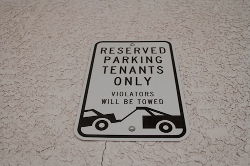 A parking sign attached to a textured wall, indicating reserved parking for tenants only. It warns that violators will be towed and features a graphic of a tow truck.