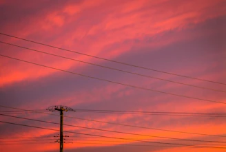 A vibrant sunset behind towering electrical power lines stretching across Indonesia's landscape.