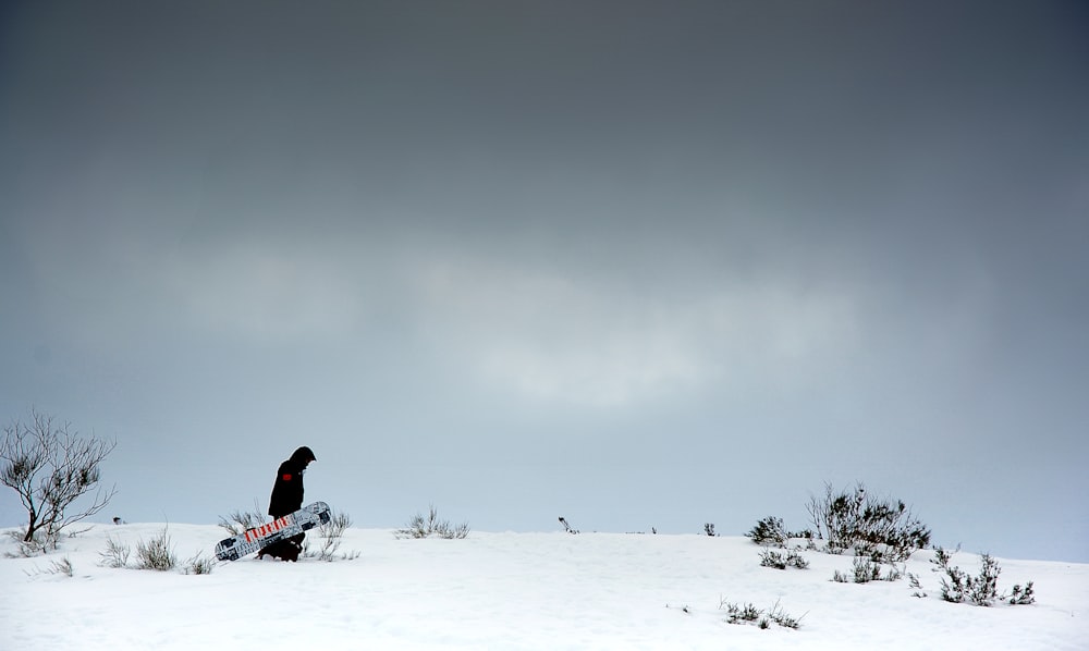 man carrying snowboard in snow field