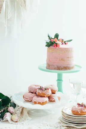 A pastel pink layered vanilla cake decorated with delicate edible flowers on a rustic wooden table.