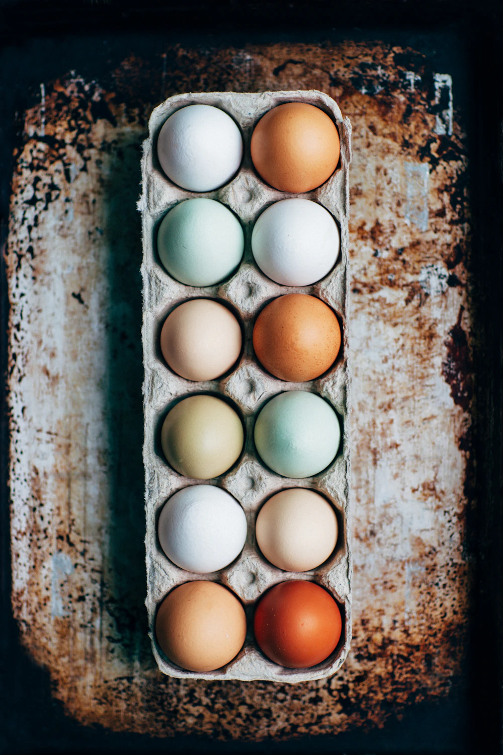 A carton of eggs in naturally different colors — white, brown, cream, and pale green