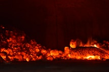 Glowing embers and charred wood pieces radiate a vibrant orange and red hue, creating an intense and warm atmosphere within a dimly lit setting.
