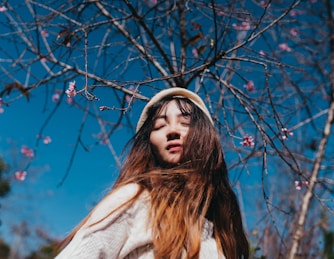 woman wearing gray sweater standing near pink petaled flowers