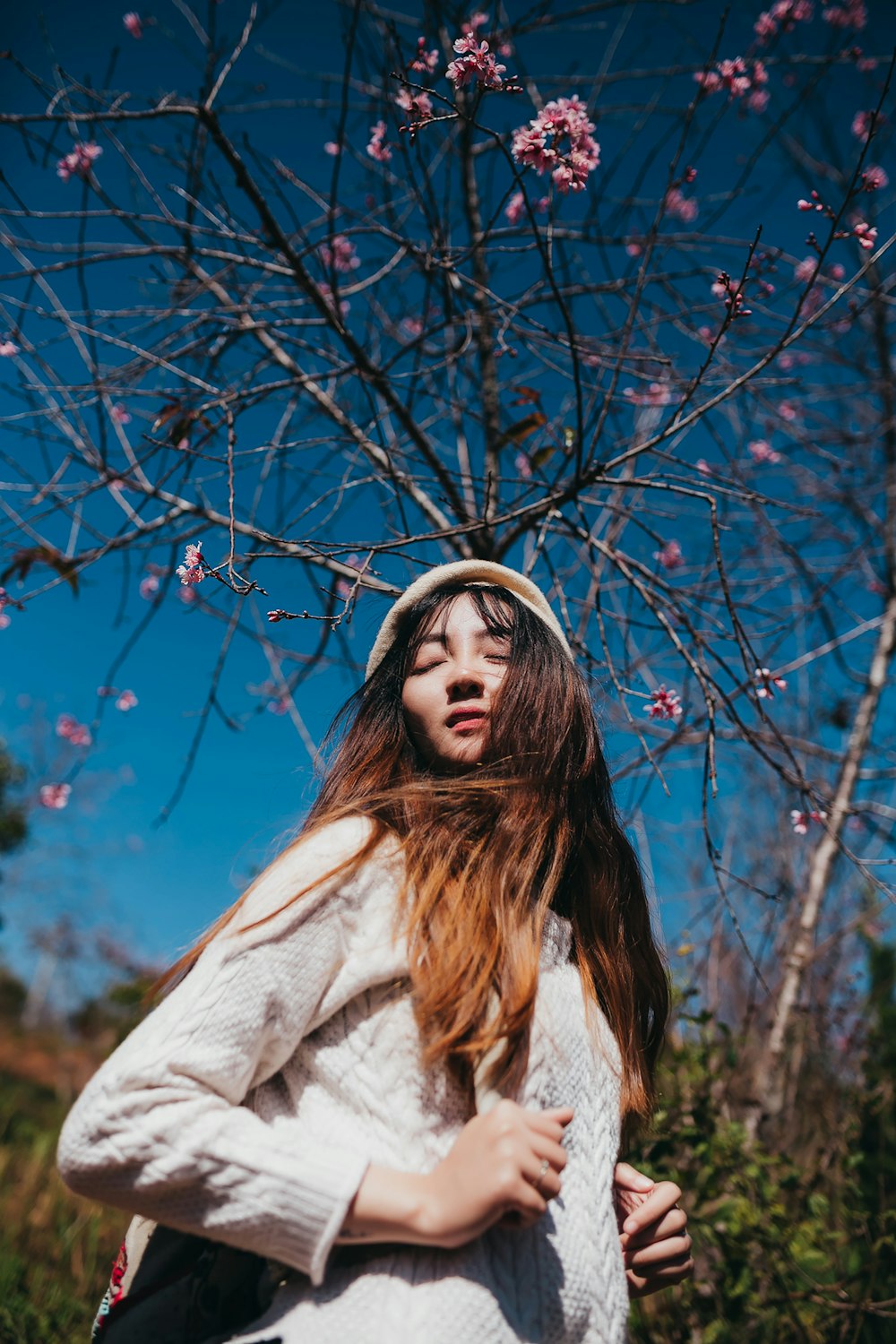 Mujer con suéter gris de pie cerca de flores de pétalos rosados